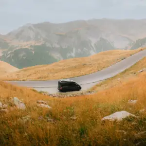Black van on a winding mountain road representing a premium round trip cab service in Hubli for outstation vacations.
